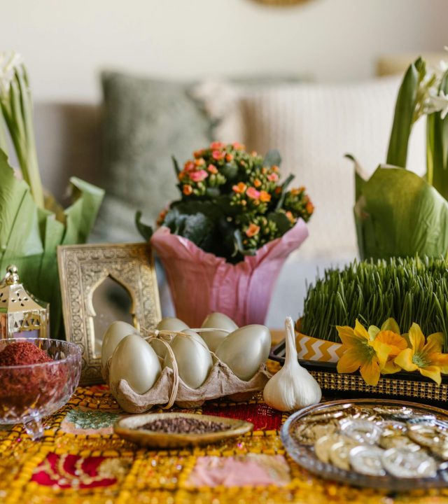 A vibrant arrangement of Nowruz haft-seen elements featuring greenery, flowers, and traditional items.